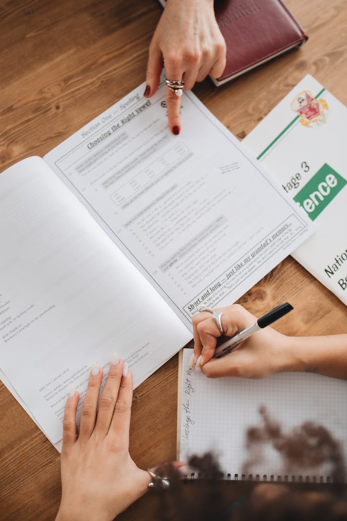 Close-up of students writing notes from an open book during a study session.