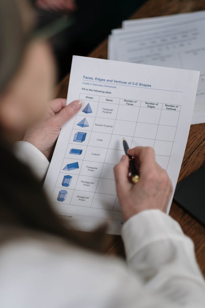 Close-up of a student filling out a geometry worksheet on 3D shapes at home.